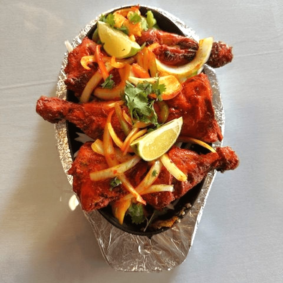 Indian Tandoori Chicken, garnished with onions, cilantro, and lime wedges, served in a sizzling platter.