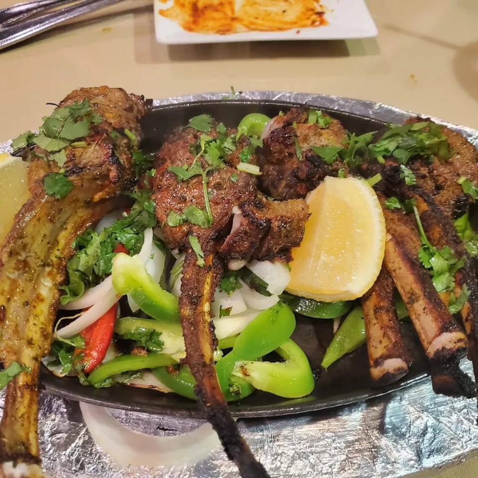 Sizzling Royal India Restaurant lamb chops with bell peppers, onions, cilantro, and lemon wedges.