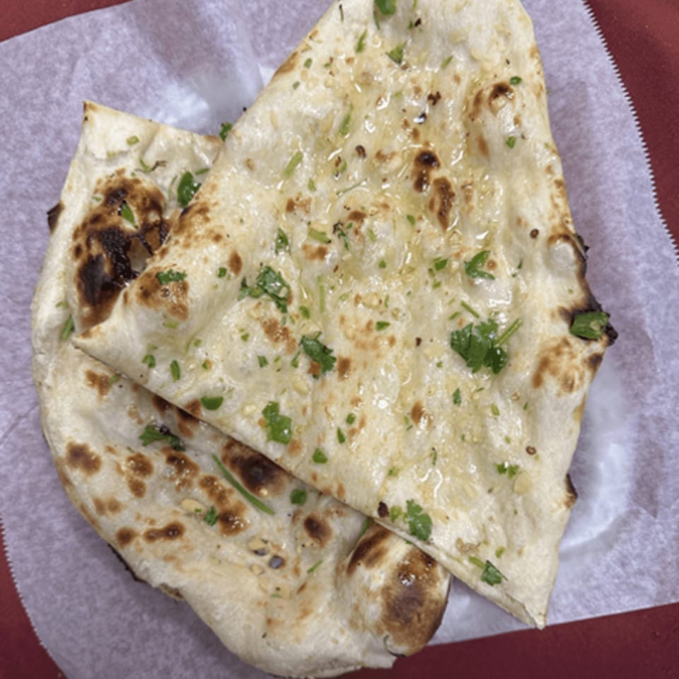 Two pieces of Royal India Restaurant's garlic naan, garnished with cilantro and butter, on white paper.