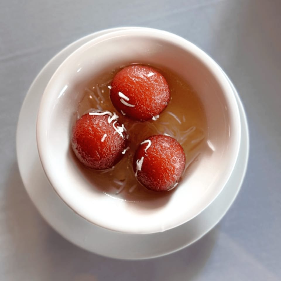 Three gulab jamun, Indian fried dough balls, in syrup with shredded coconut in a white bowl.