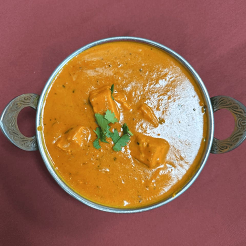 Royal India Restaurant's paneer butter masala, a rich orange curry with paneer cubes and cilantro in a metal bowl.