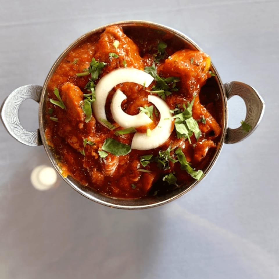 Indian curry in a silver bowl, garnished with fresh cilantro and white onion rings.