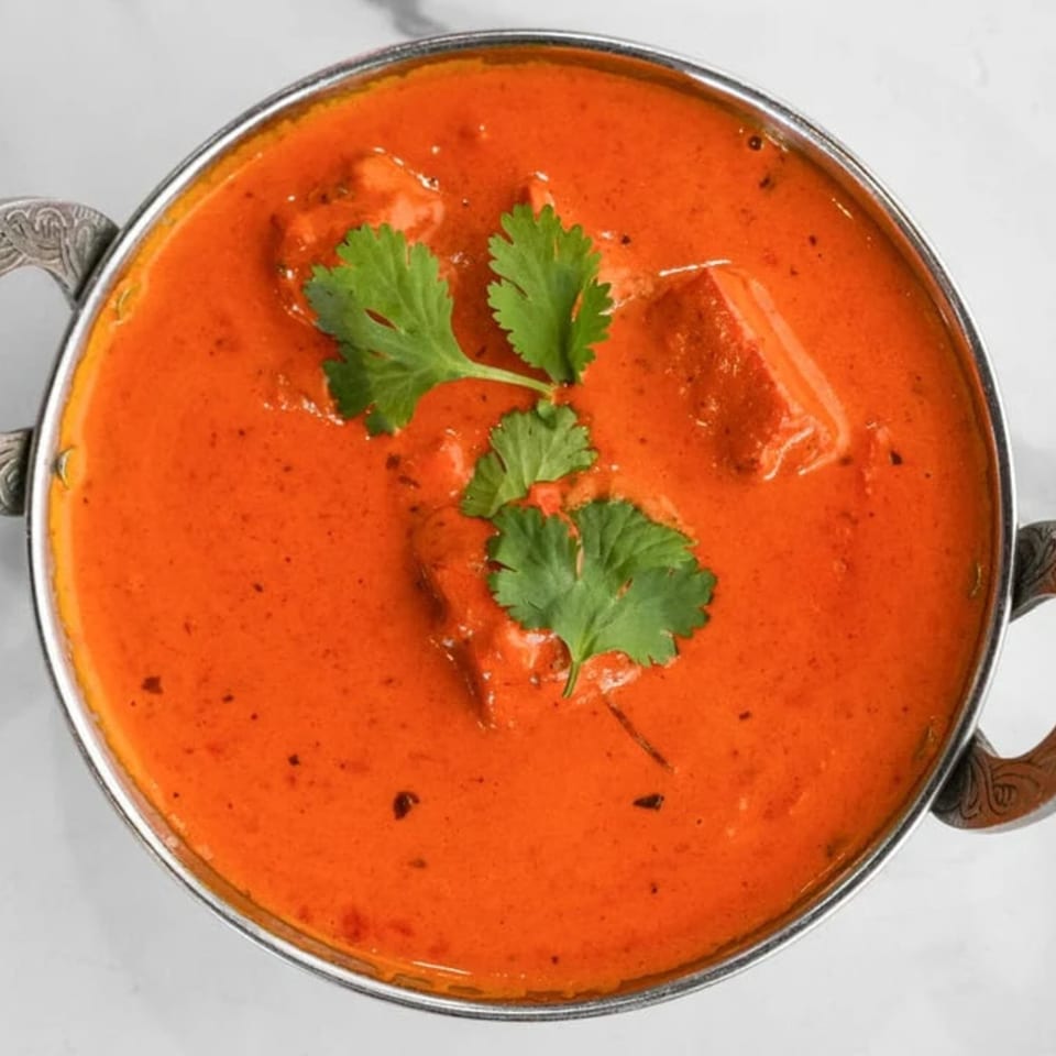 Royal India Restaurant's vibrant orange Indian curry, garnished with fresh green cilantro in a metal bowl.