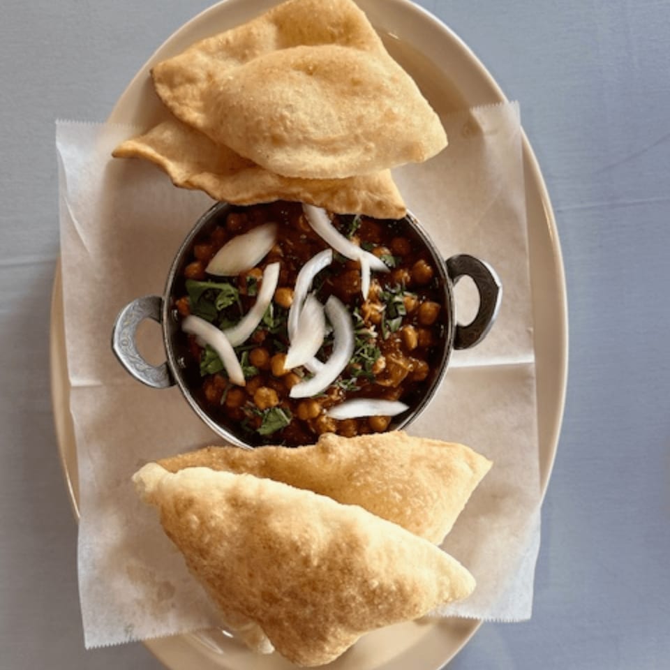 Chana Masala with sliced onions and cilantro, served with fluffy puri bread on a plate.